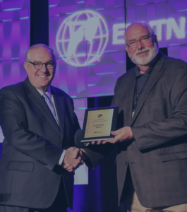 Two men smiling and holding a St Michael Radio recognition prize together.